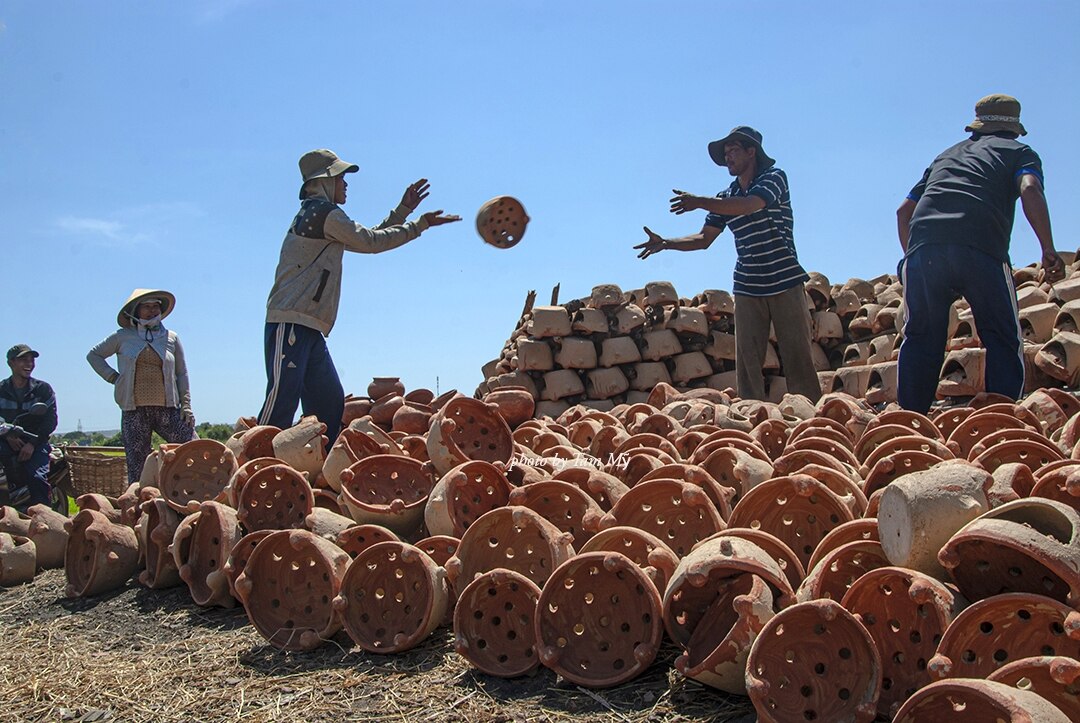 Các nghệ nhân làng Bình Đức đang sắp xếp sản phẩm gốm gia dụng để nung ngoài trời.