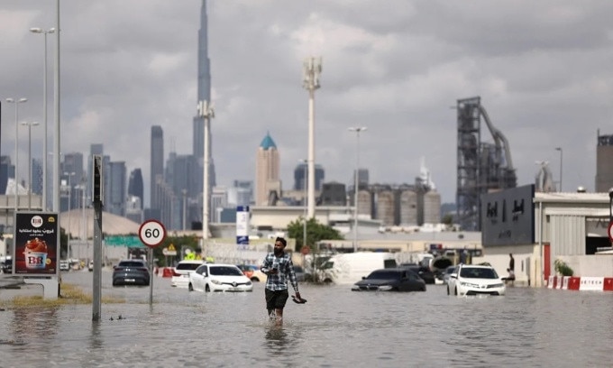 Người đàn ông bước đi trong nước lũ, phía sau là tòa tháp Burj Khalifa ở Dubai, UAE, hôm 17/4. Ảnh: Reuters