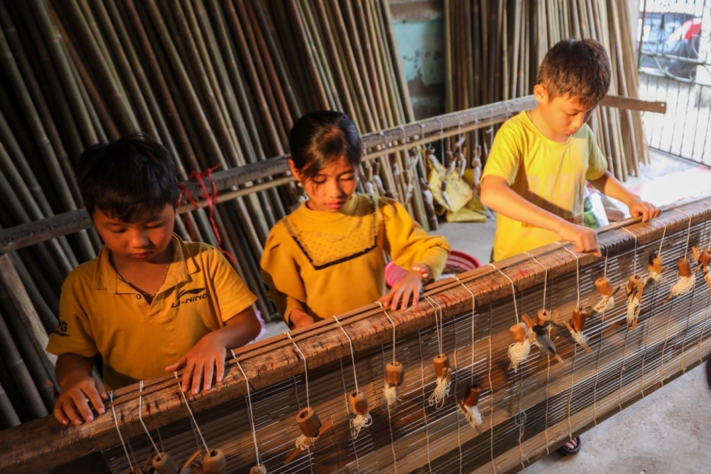 Tranh thủ ngày hè các em nhỏ ở làng nghề làm mành truyền thống thôn Đa Quang, xã Dị Chế, giúp gia đình làm mành tre