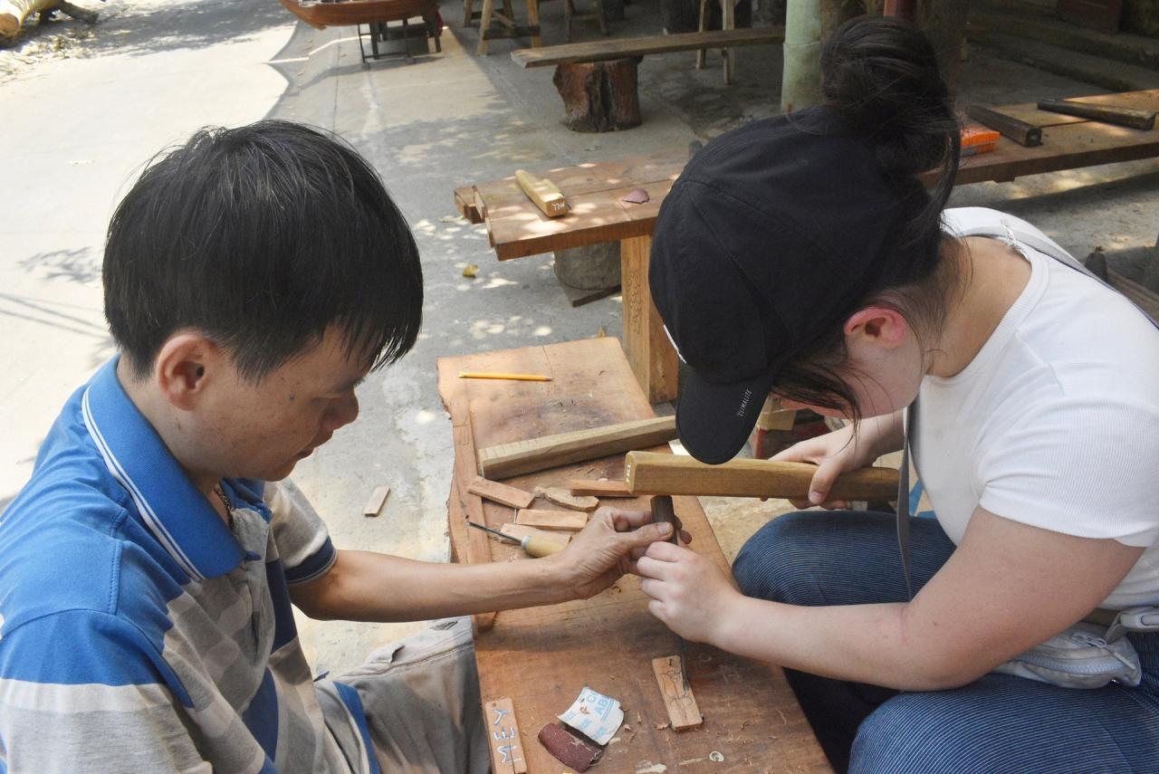 M. Thi guide avec enthousiasme les touristes sur la façon de sculpter le bois. Photo : N.Q