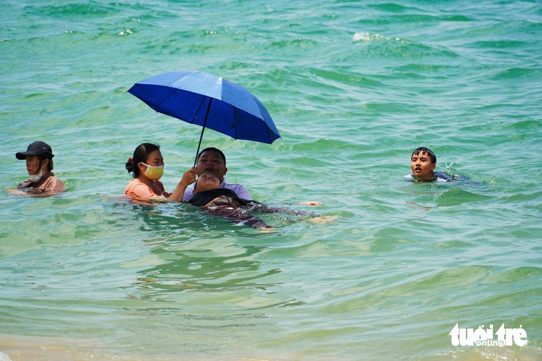 Nhiều người vừa che dù vừa tắm biển để tránh nắng - Ảnh: TRẦN HOÀI